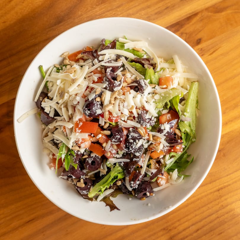 Overhead view of a salad with mixed greens, tomatoes, olives, sunflower seeds, and shredded cheese.