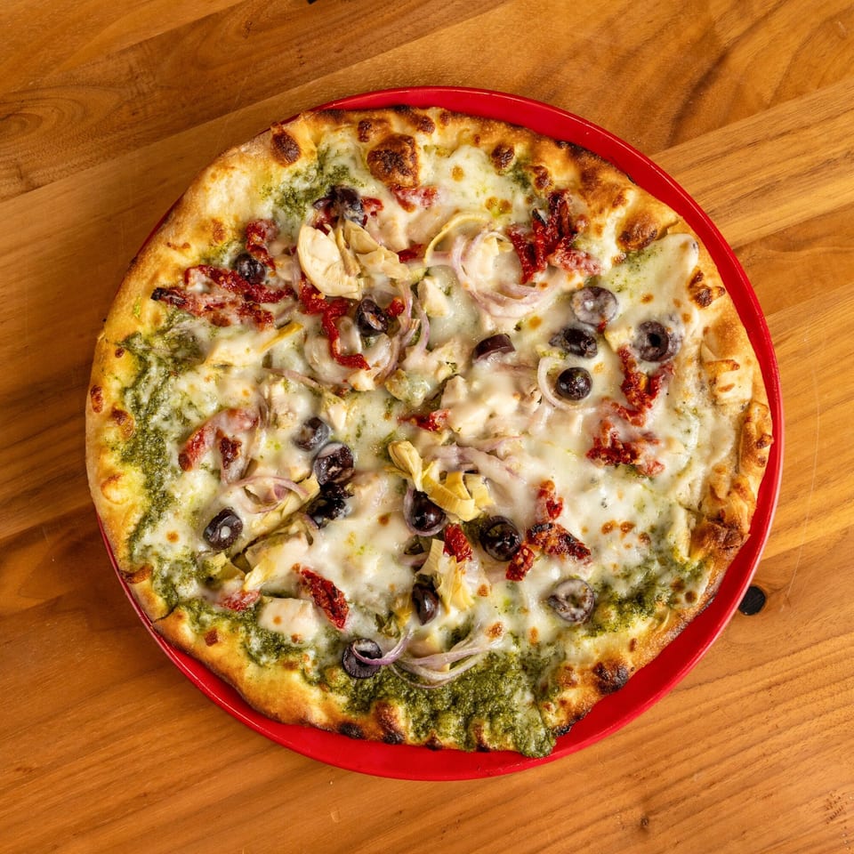 A pesto pizza with mozzarella, sun-dried tomatoes, black olives, red onions, and artichoke hearts.